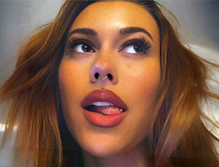 a woman looking upward, with a septum ring, a small stud above her lip, and a curved barbell snake eyes piercing on the tip of her tongue.