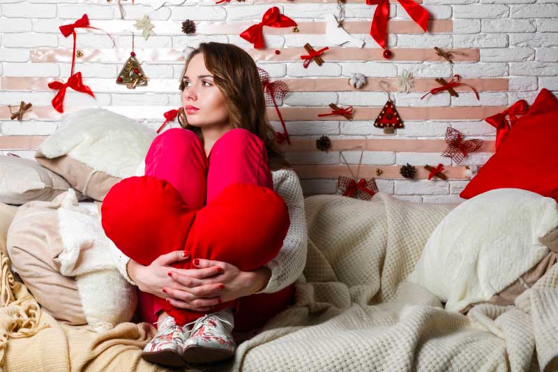 Sad unhappy woman holding red heart pillow