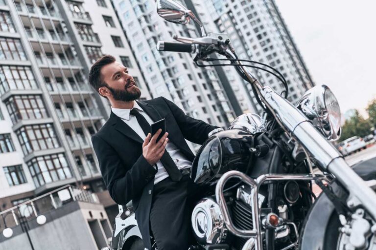 Lawyer in a suit using smartphone by a motorcycle in an urban setting.