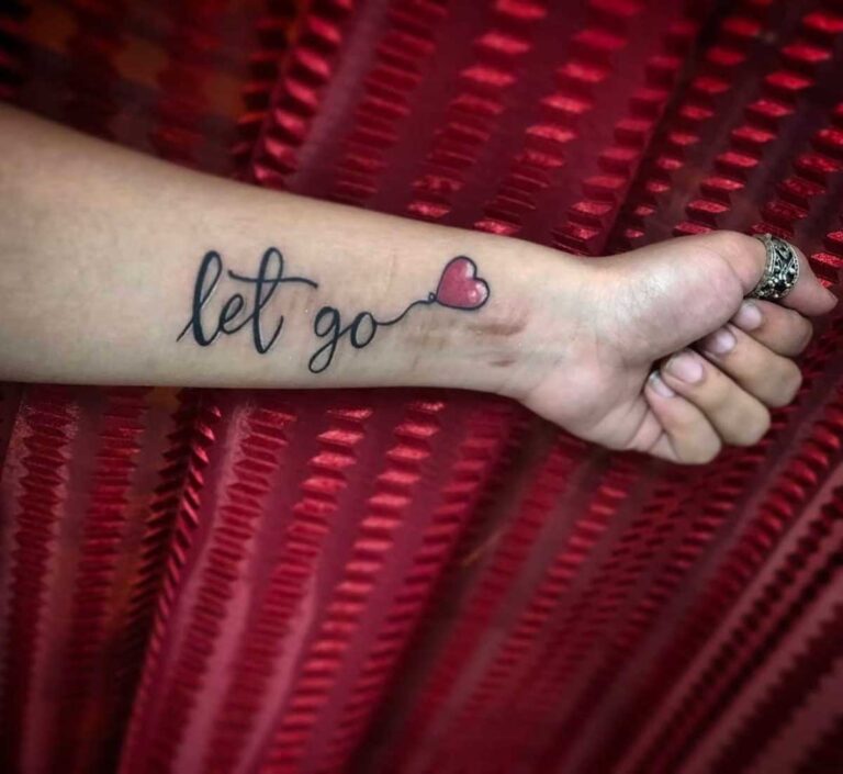 Close-up of a 'let go' tattoo with heart on forearm against red fabric background.