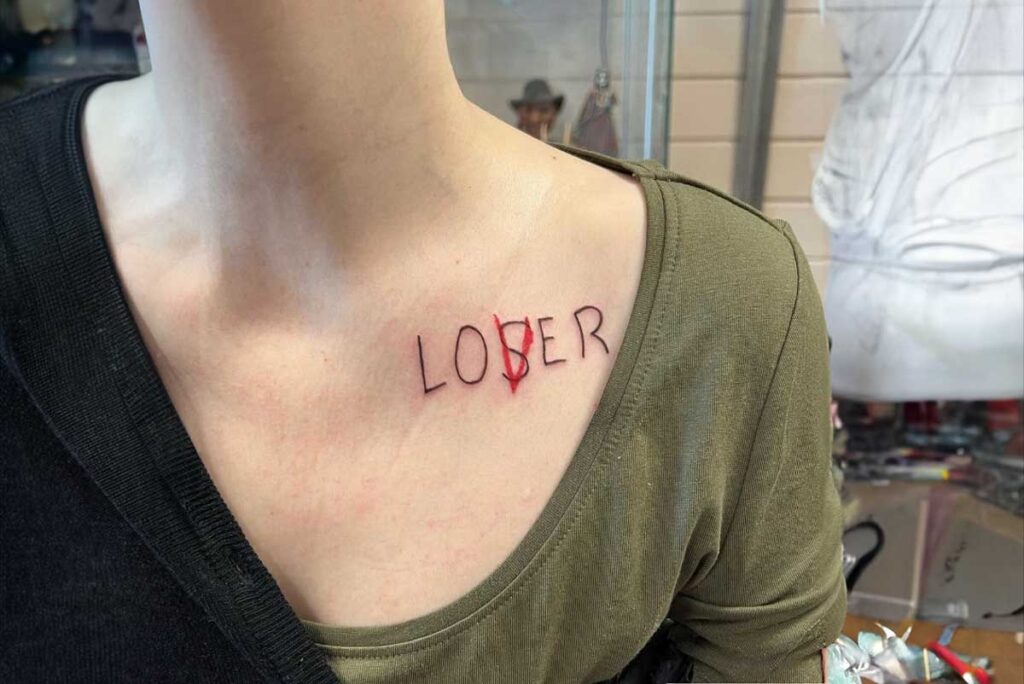 Close-up of a neck with a 'loser lover' tattoo, the 's' in red, symbolizing lost love and regret.