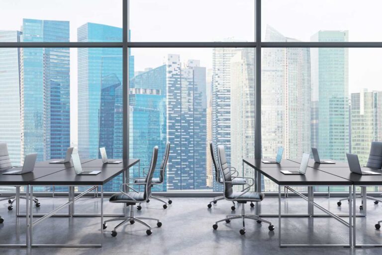 Modern shared office space with laptops on desks and panoramic city skyline view.