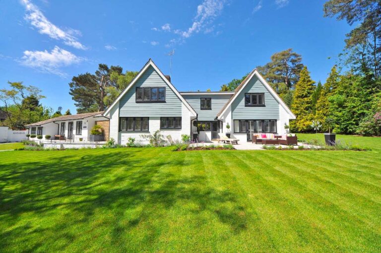 Charming two-story house with white and green facade, manicured lawn, and lush garden.
