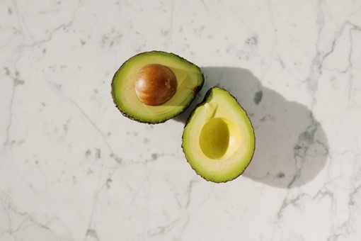 Ripe avocado halved with pit on white marble background, top view