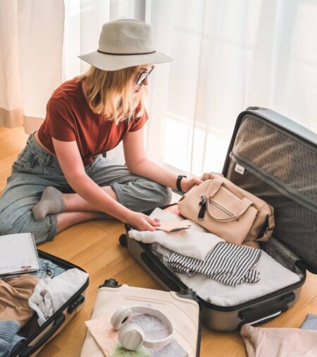 A young woman sitting on the floor surrounded by suitcases. She is packing clothing and accessories into an open suitcase.