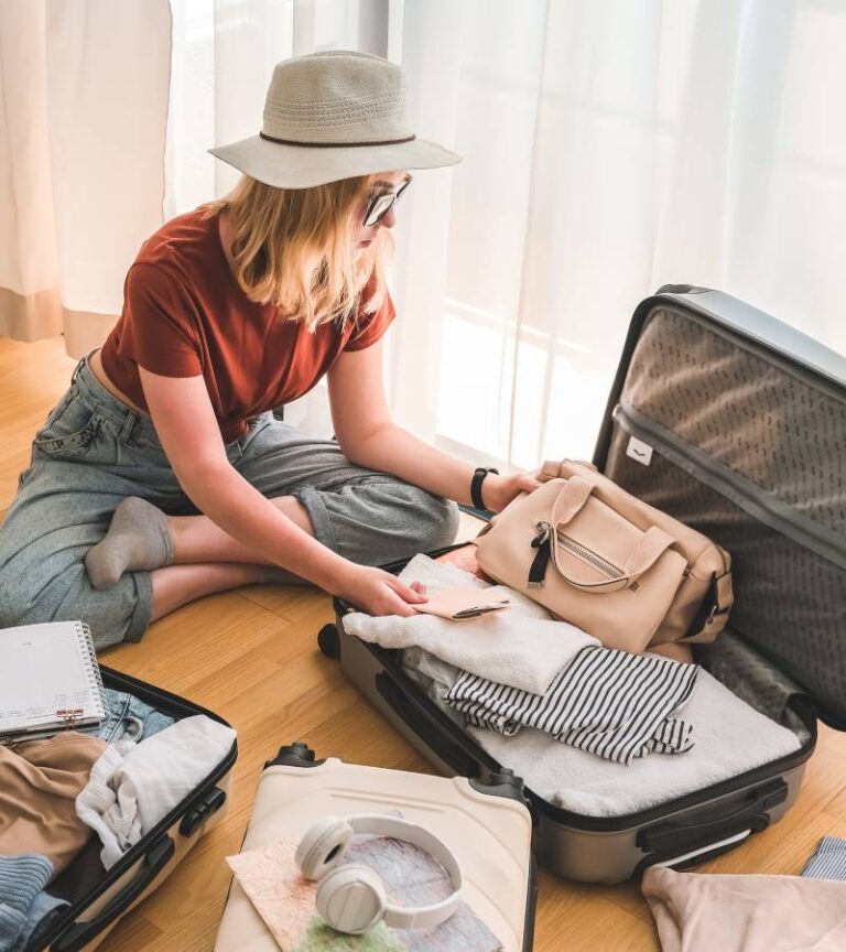 A young woman sitting on the floor surrounded by suitcases. She is packing clothing and accessories into an open suitcase.