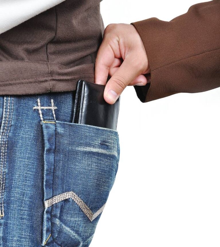 A pickpocket reaches his hand into the back pocket of a pair of jeans and attempts to steal the victim's black wallet.