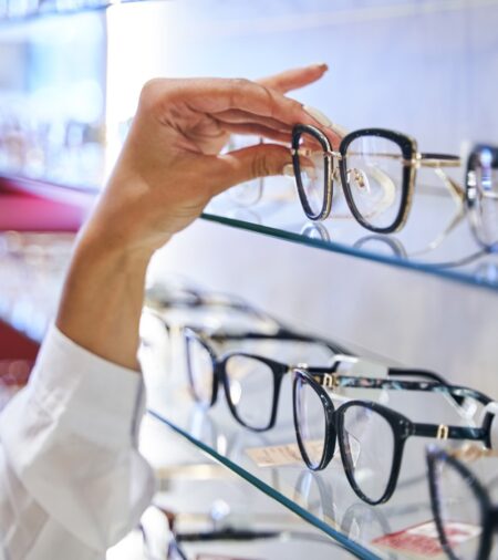 A person at the eyeglass wall hand selecting a stylish pair of frames to try on. They're getting new glasses.