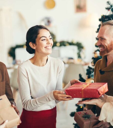 A close-up of a diverse group of friends, smiling and exchanging gifts at a professional holiday party.