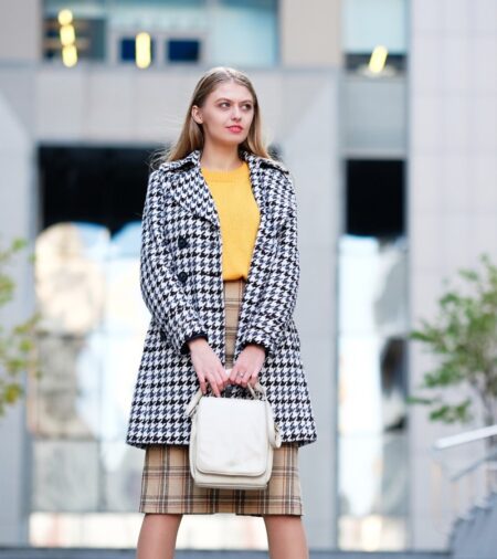 A professional working woman standing on the steps outside. She's wearing a houndstooth jacket and plaid skirt.