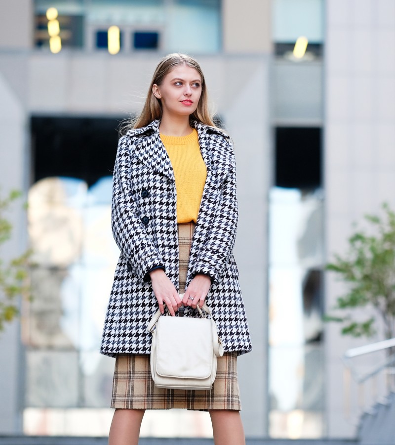 A professional working woman standing on the steps outside. She's wearing a houndstooth jacket and plaid skirt.