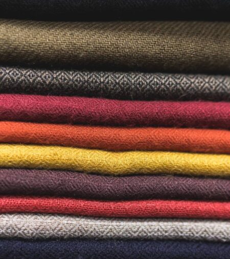 A stack of fabric folded neatly on a table. Each piece of fabric is a different earth tone shade from red to brown.