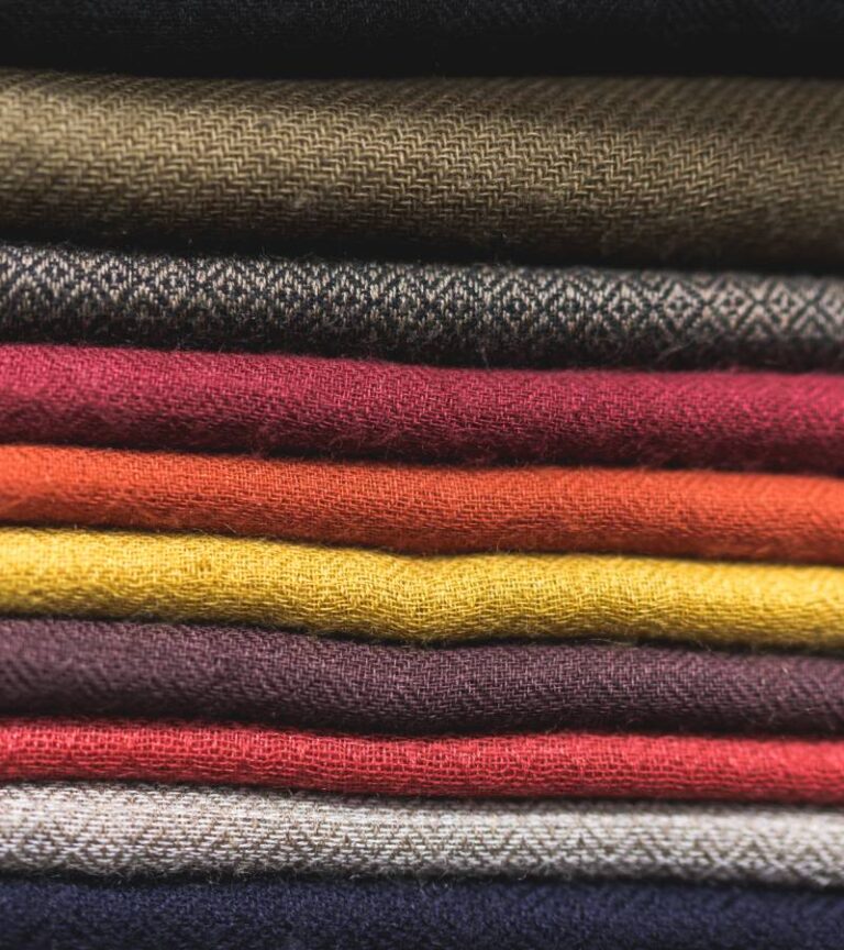A stack of fabric folded neatly on a table. Each piece of fabric is a different earth tone shade from red to brown.