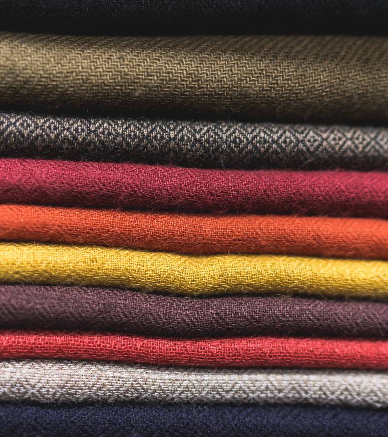 A stack of fabric folded neatly on a table. Each piece of fabric is a different earth tone shade from red to brown.