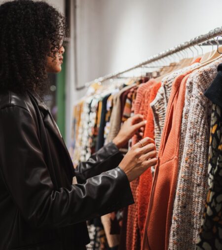 A woman wearing a leather jacket in front of a clothing rack. The rack has various long- and short-sleeved shirts.
