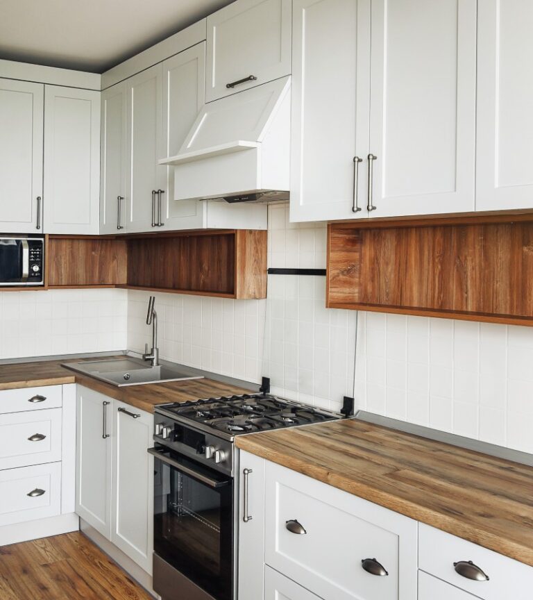A modern Scandinavian kitchen with butcher block countertops, white cabinets, and stainless steel appliances.
