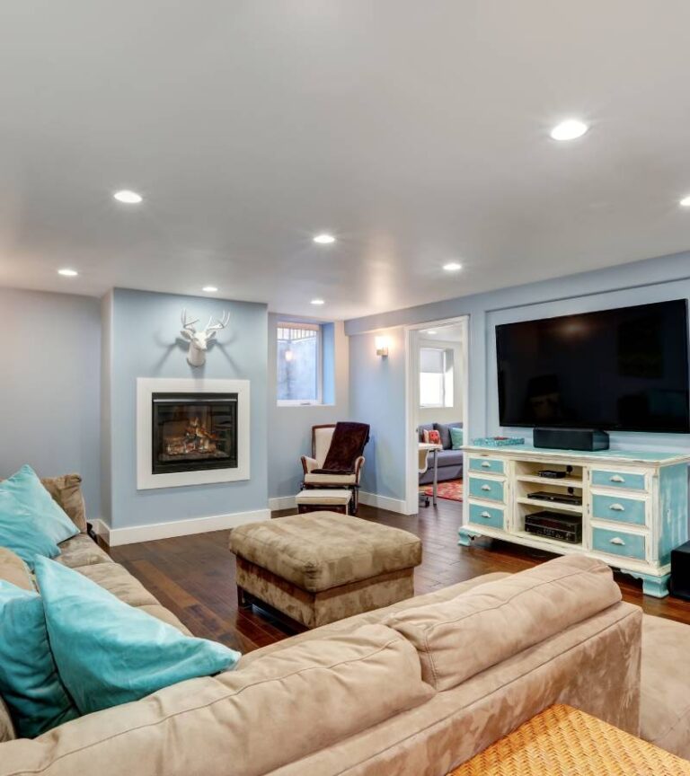 A basement with pastel blue walls and white trimming. The space has a couch, entertainment center, and fireplace.