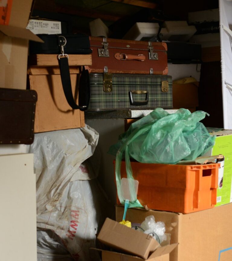 A large cluttered storage area filled with various things. Luggage, plastic tubs of clothes, and boxes fill the space.