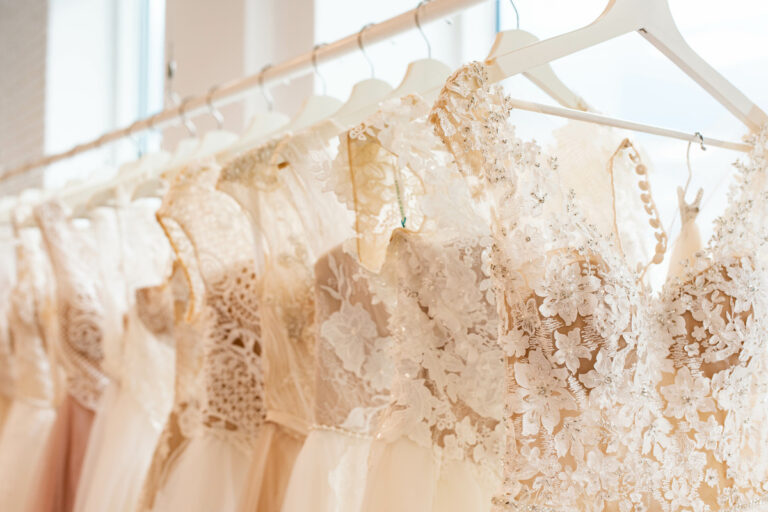 A garment rack with a row of wedding dresses hanging on white hangers. The gowns are lace, tulle, and beaded.