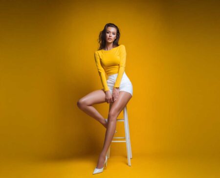 A female model, dressed in a yellow long sleeved T-shirt and white shorts.