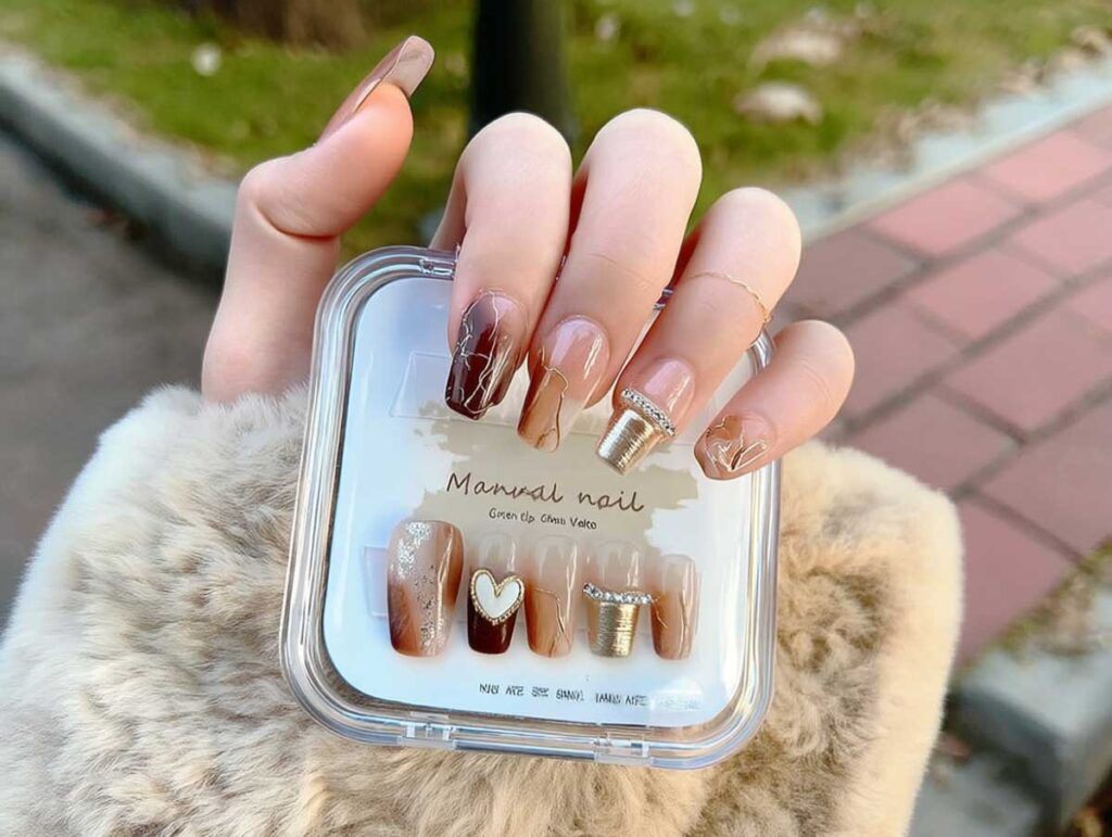 Close-up photo of a left hand, wearing a beige faux-fur coat sleeve, holding a clear square case of press-on nails