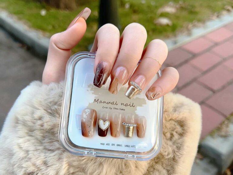 Close-up photo of a left hand, wearing a beige faux-fur coat sleeve, holding a clear square case of press-on nails