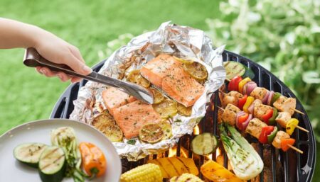 A hand is using tongs to turn a large piece of salmon on a grill.